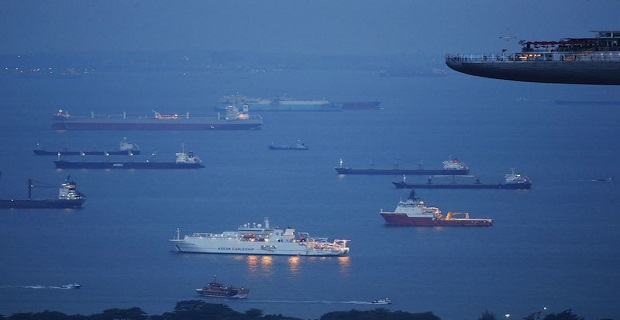 Ships anchor outside the harbour as they wait to berth at a port terminal, near the skydeck of the Marina Bay Sands hotel and casino, in Singapore